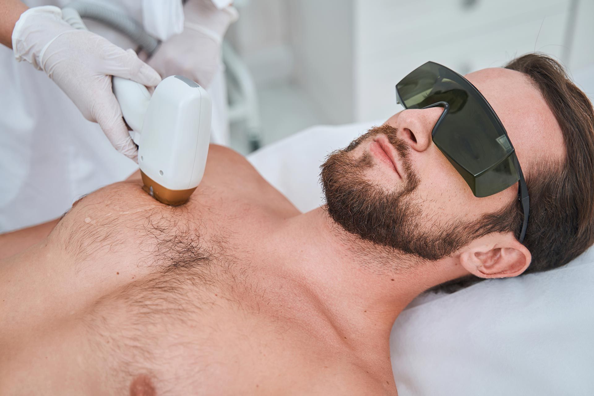 Laser hair removal treatment on a man's chest while he lies on a white treatment bed.