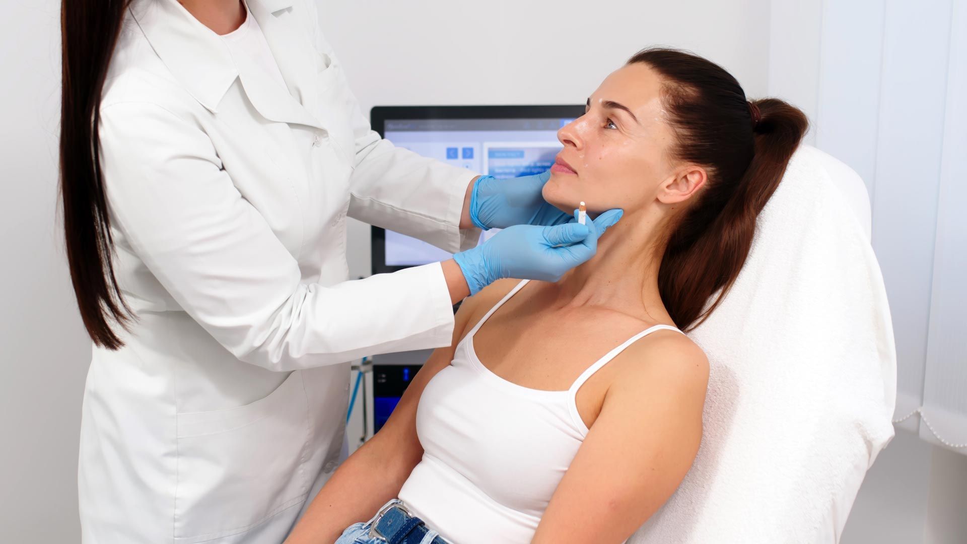 Doctor wearing blue gloves examines a woman’s chin in a clinic chair