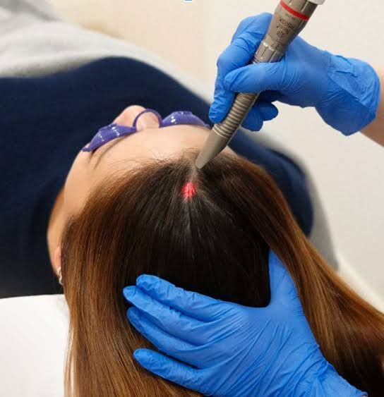 A woman receives a facial treatment with gloved hands applying a blue device and yellow applicator.