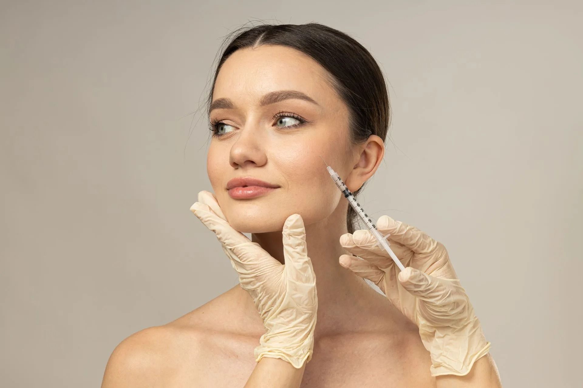 Gloved hands inject filler into a woman’s cheek in a clinical beauty treatment setting