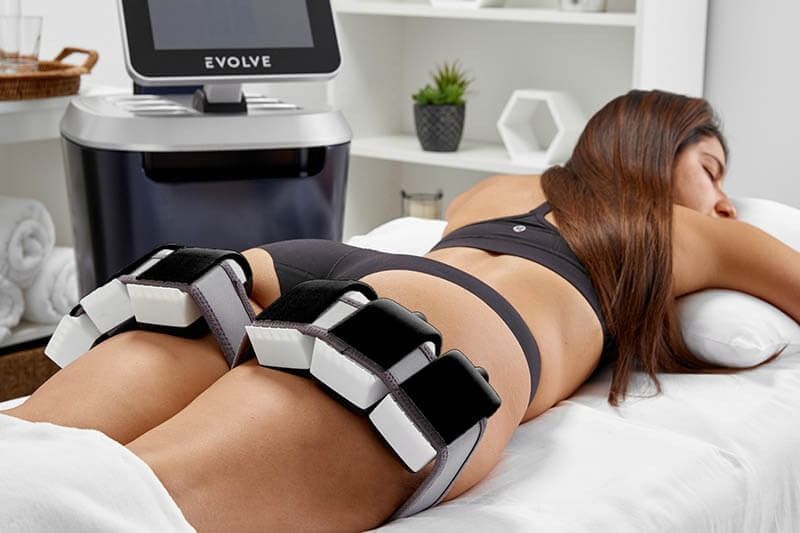 Person lying on a bed during a leg massage with a black-and-silver EMS stimulation device