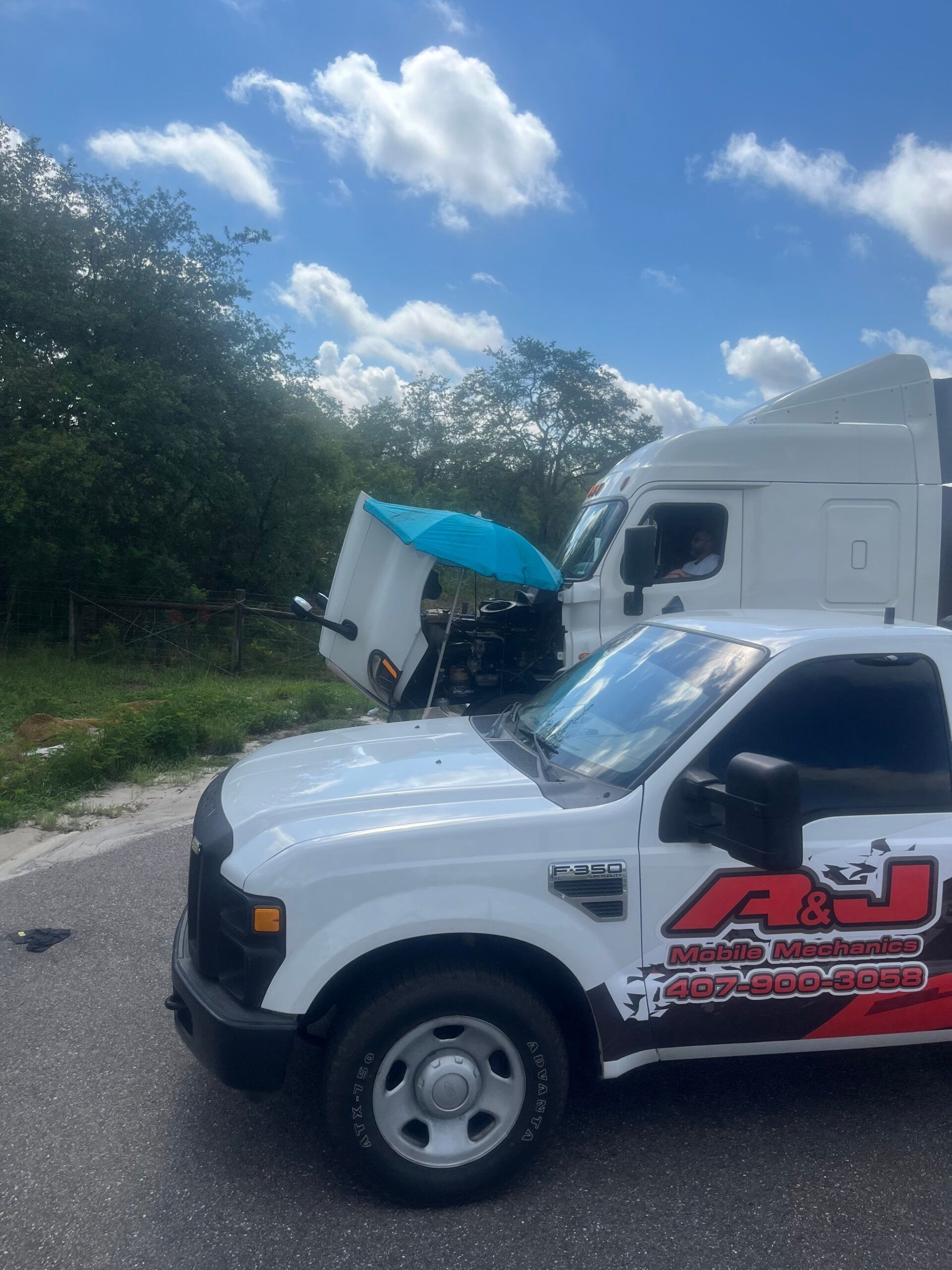A white truck with the hood up is parked next to a semi truck.