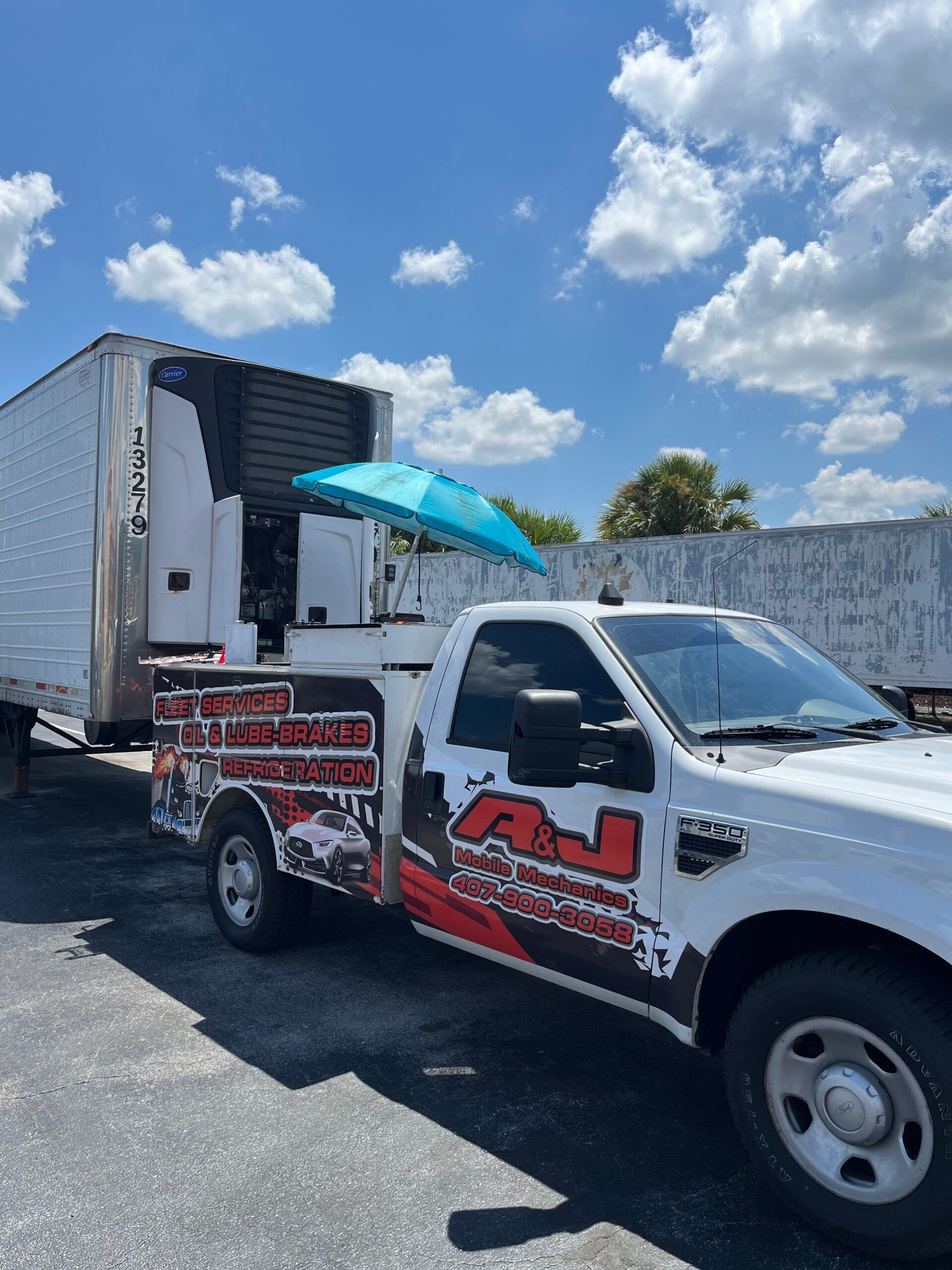 A white truck with a blue umbrella on the side is parked next to a trailer.