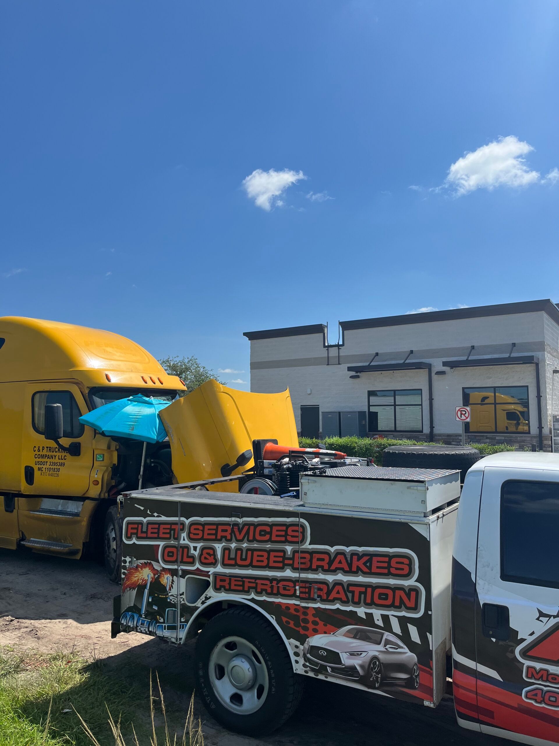 A tow truck is parked next to a yellow semi truck with the hood open.