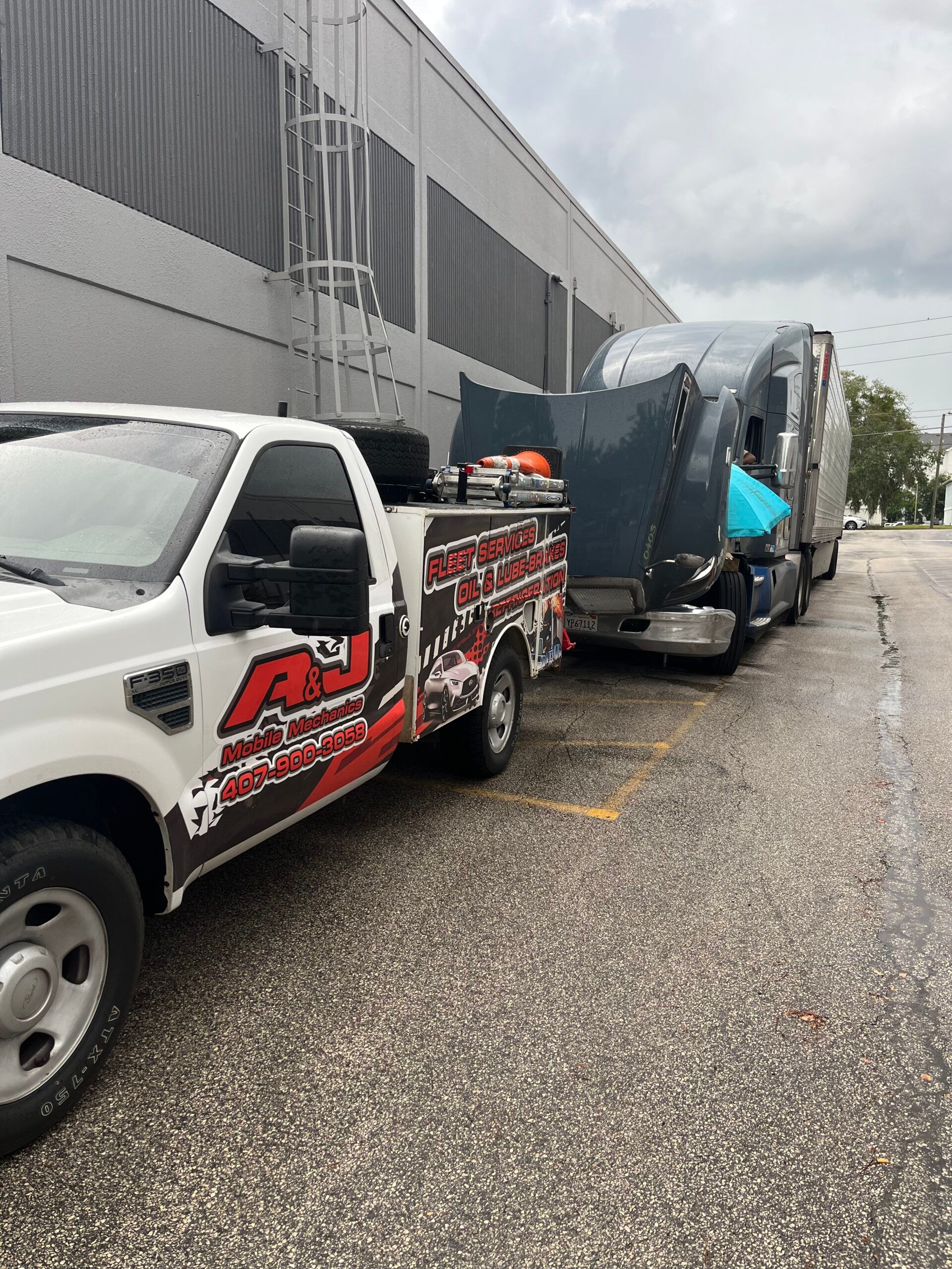 A tow truck is towing a semi truck in a parking lot.