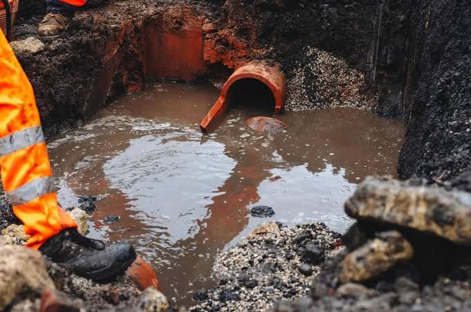Orange pipe discharging muddy water into a trench, with a worker’s boot visible at left