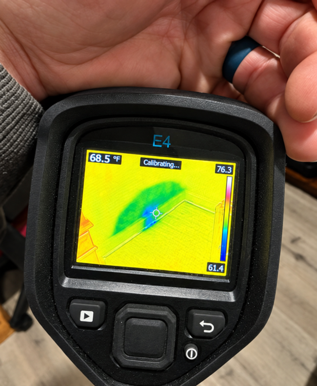 Handheld thermal camera showing a hot spot on a surface, held in one hand