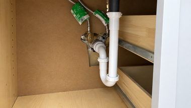 Under-sink cabinet with exposed white plumbing pipes and a green valve