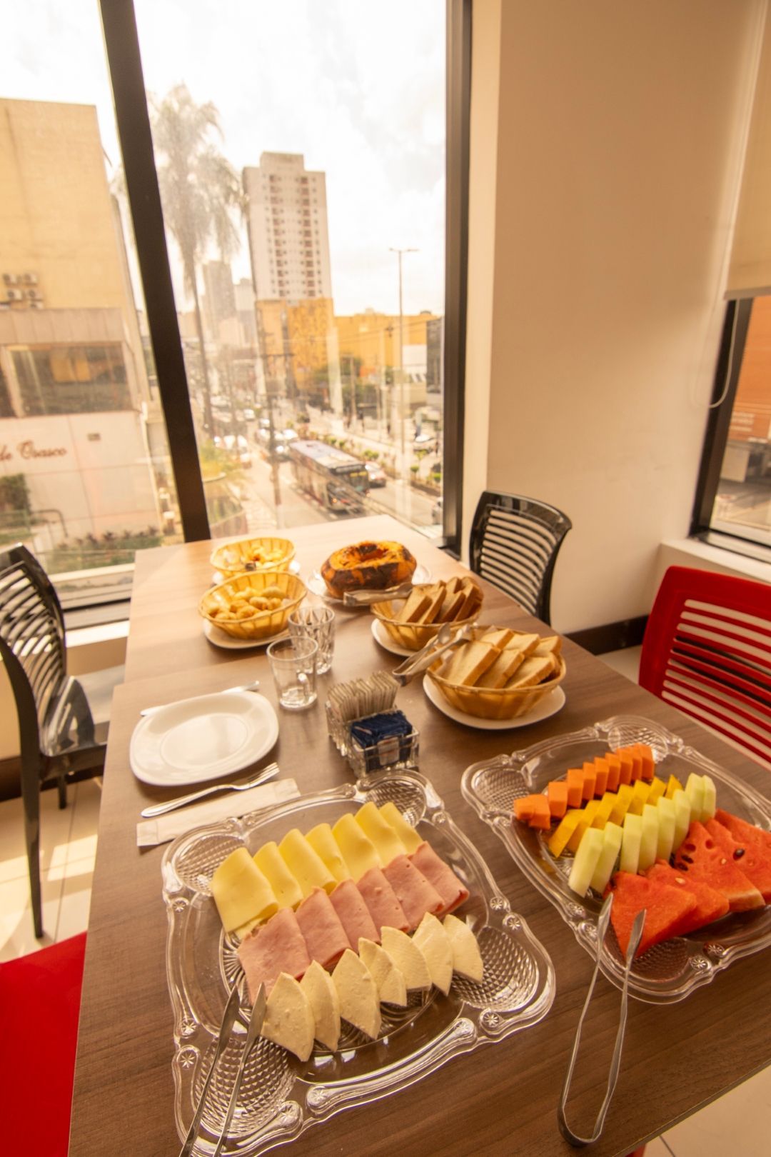 Uma mesa com pratos de comida e frutas em frente a uma janela.