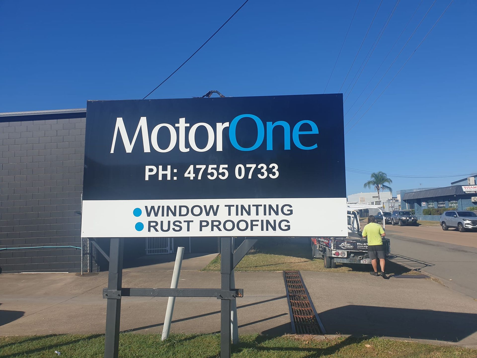 Sign for MotorOne with business details: phone number, services offered, and an employee near parked vehicles.