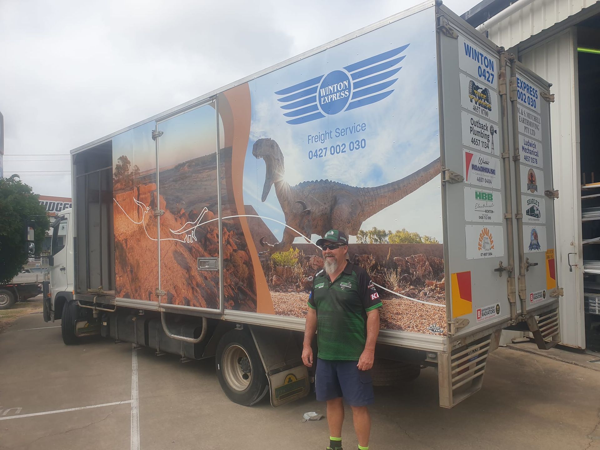 Man stands next to a truck with dinosaur graphic. The truck is open, with a landscape scene.