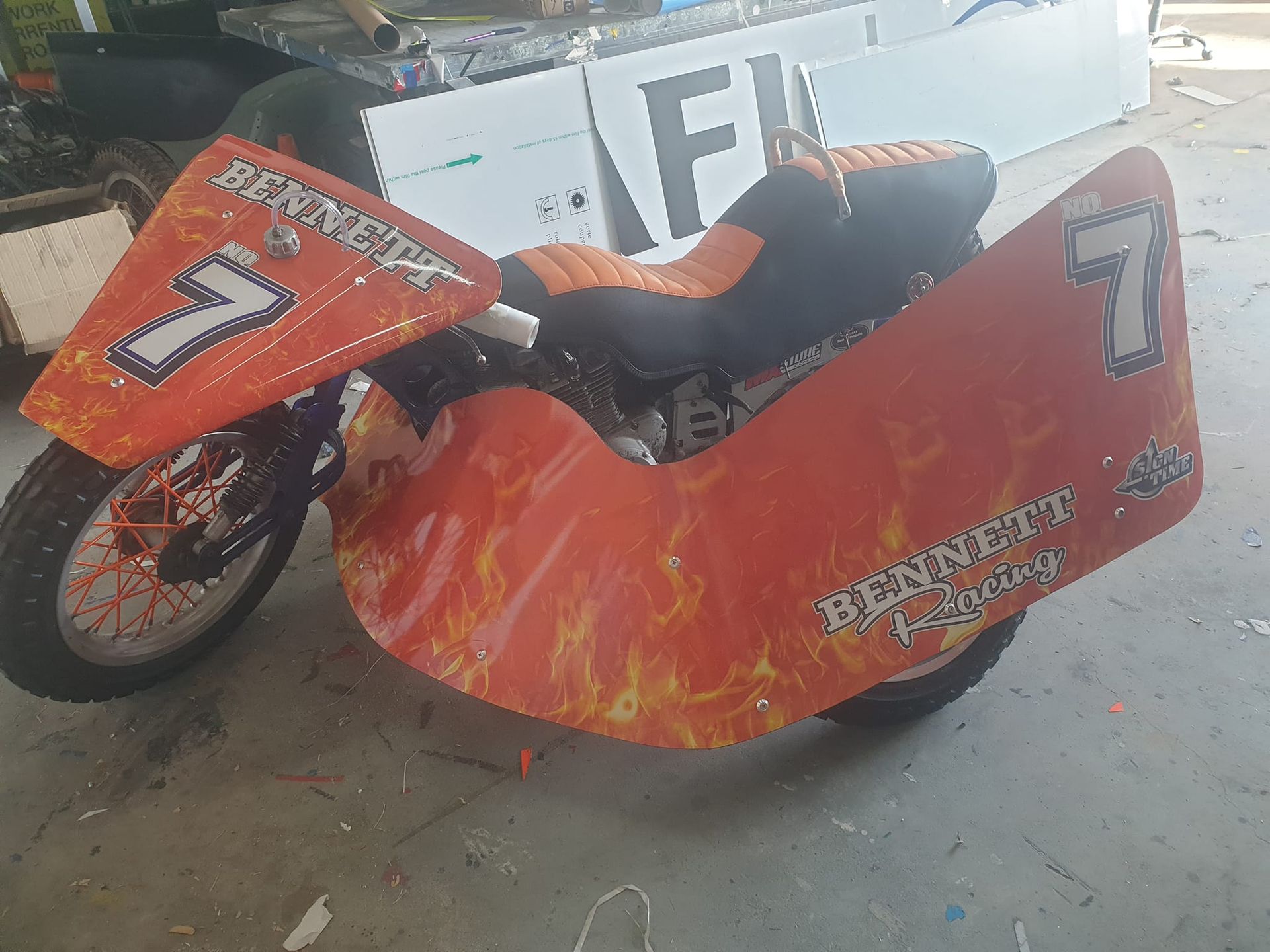 Orange and black sidecar motorcycle with the number 7, flames, and a customized seat.