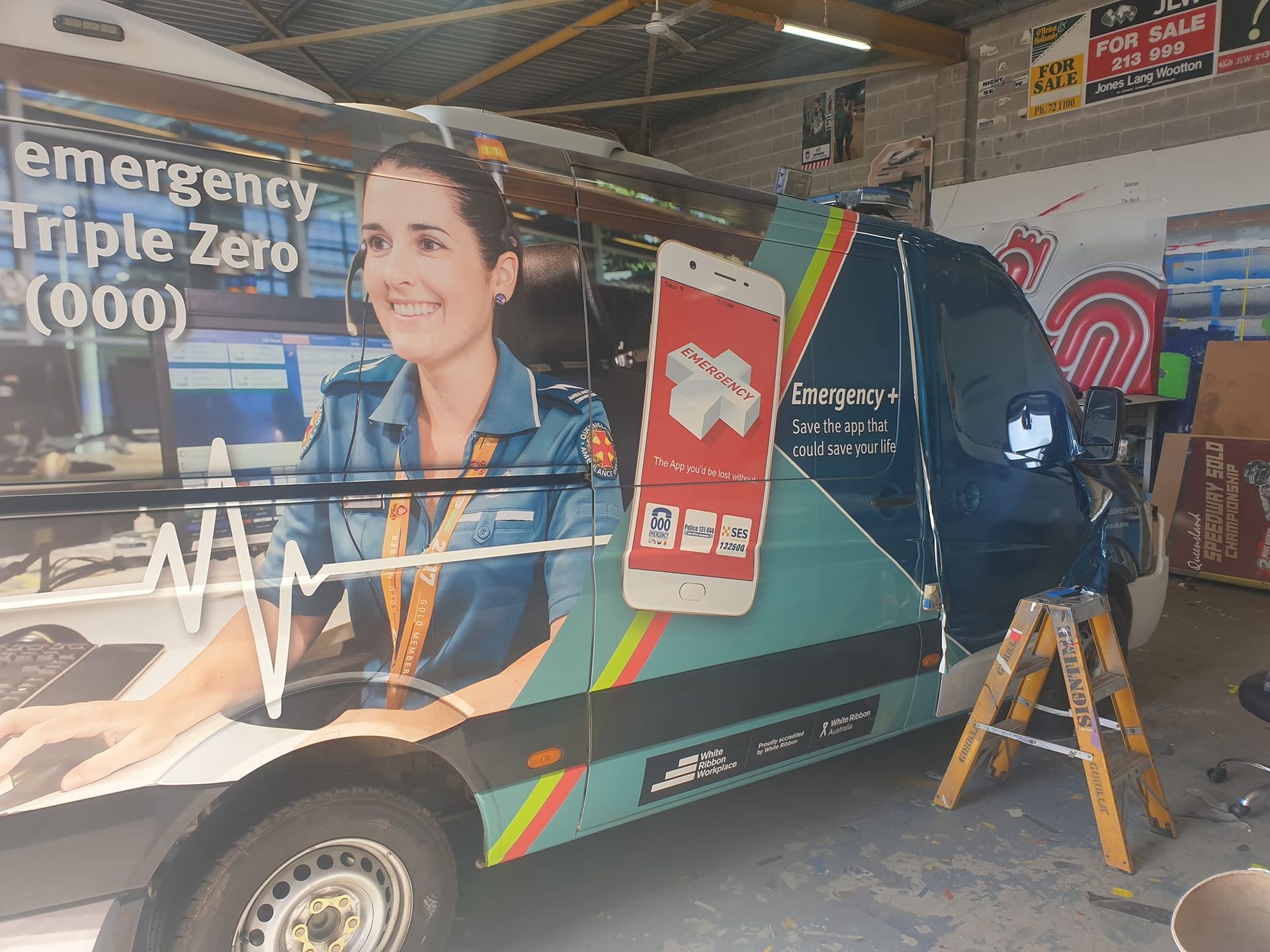 Van with emergency services graphics: a woman on the side with a phone graphic, parked in a garage.