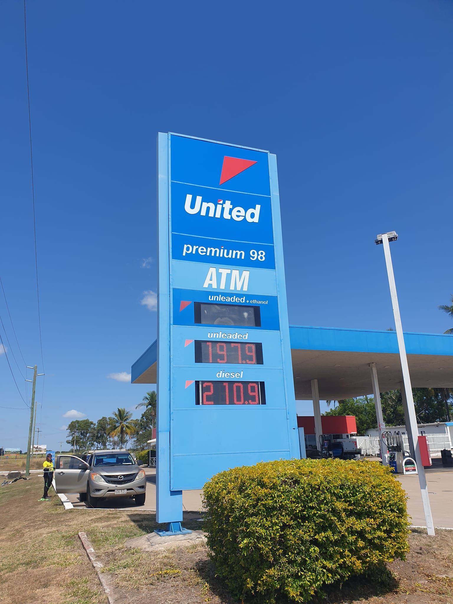 Blue United gas station sign displays fuel prices; a car and employee are present.