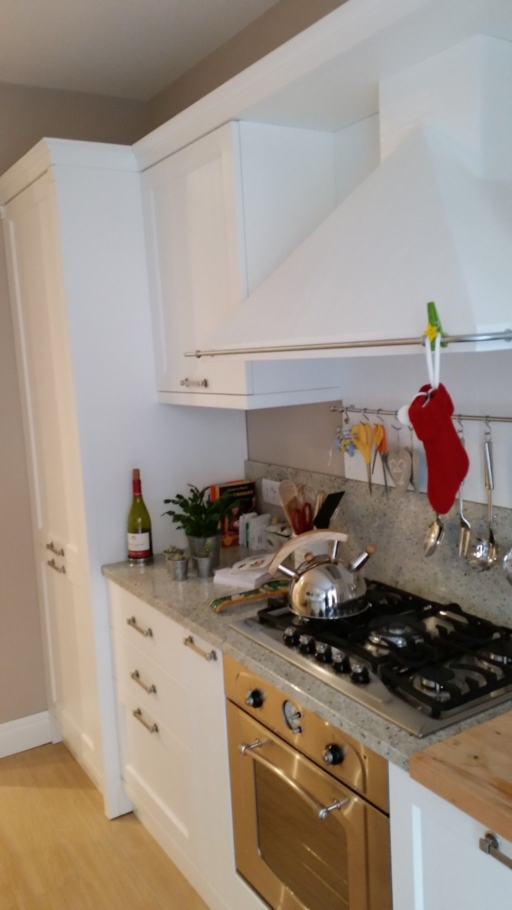 Cucina bianca con fornelli, forno, pensili e una calza rossa appesa vicino ai fornelli.