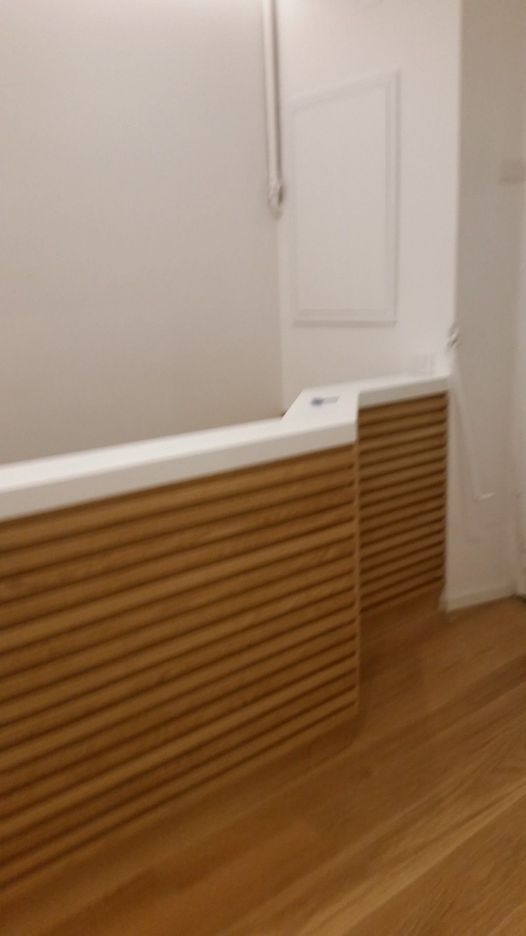 Hall moderna con bancone della reception rivestito in legno, pareti bianche e pavimento in parquet.