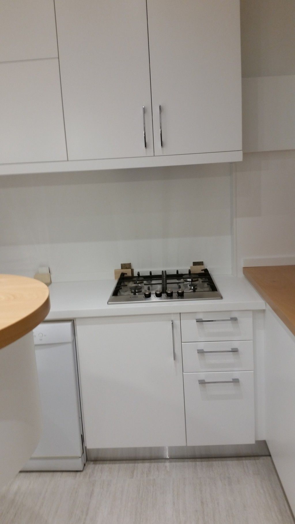 Cucina compatta con mobili bianchi, piano cottura a gas e ripiani in legno chiaro su pavimento piastrellato.