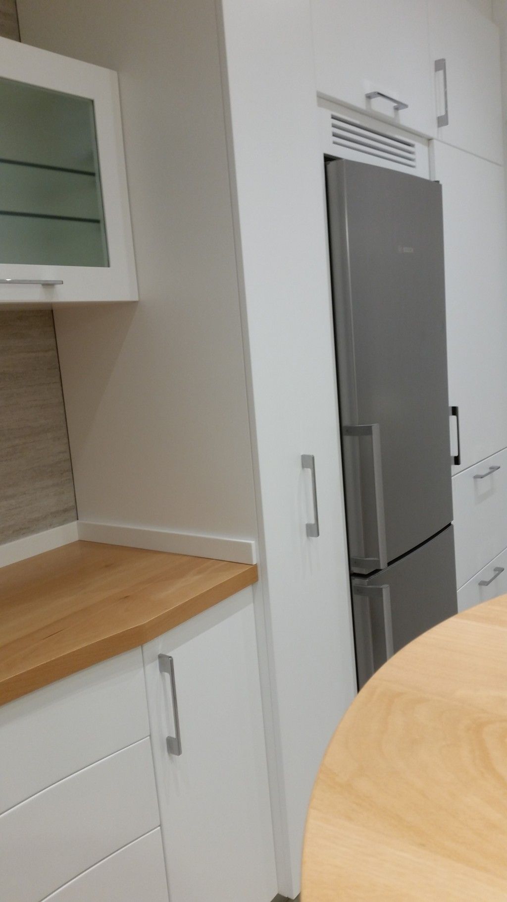 Cucina moderna con mobili bianchi, piano di lavoro in legno, frigorifero in acciaio inox e tavolo rotondo.