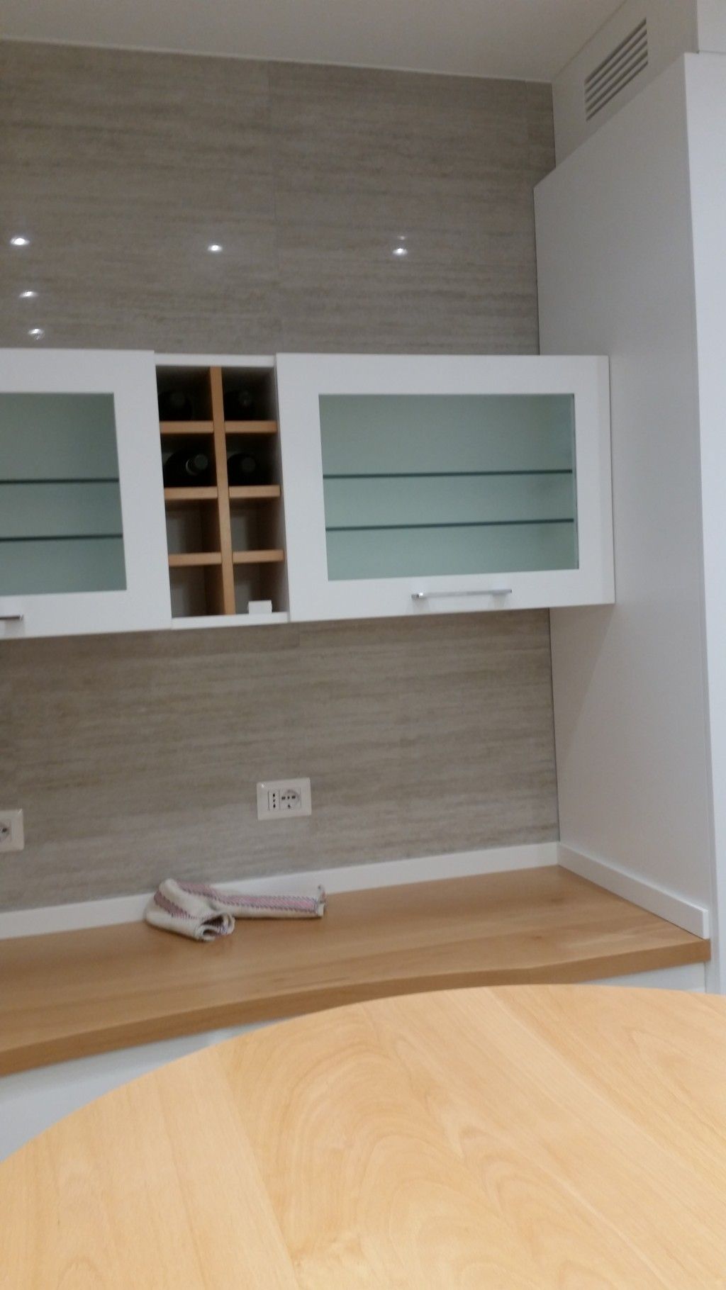 Cucina moderna con mobili bianchi, paraschizzi piastrellato in grigio, pavimento in legno e un tavolo rotondo in primo piano.