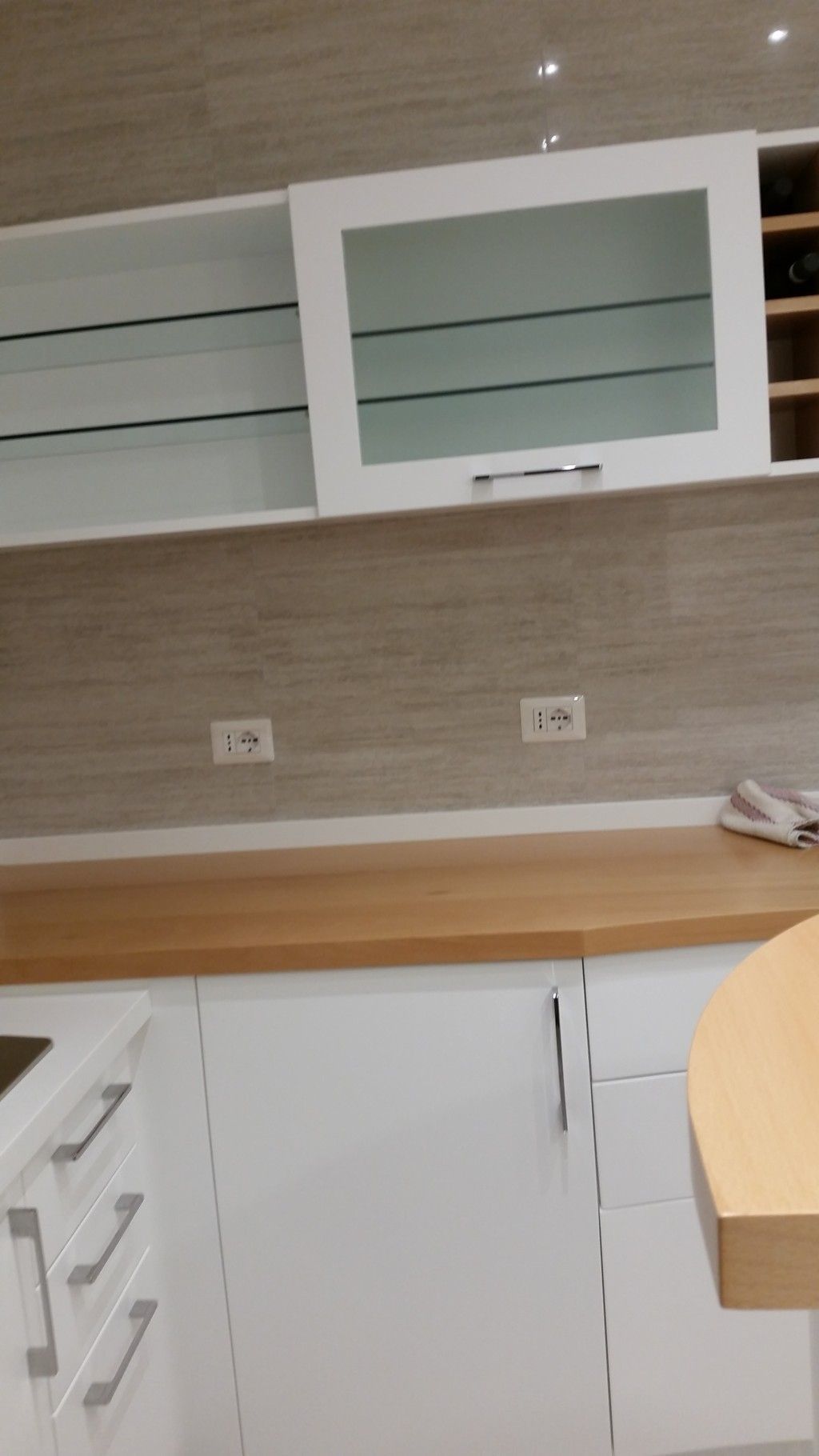 Cucina moderna con mobili bianchi, piano di lavoro in legno, mensole a vista e TV a parete.