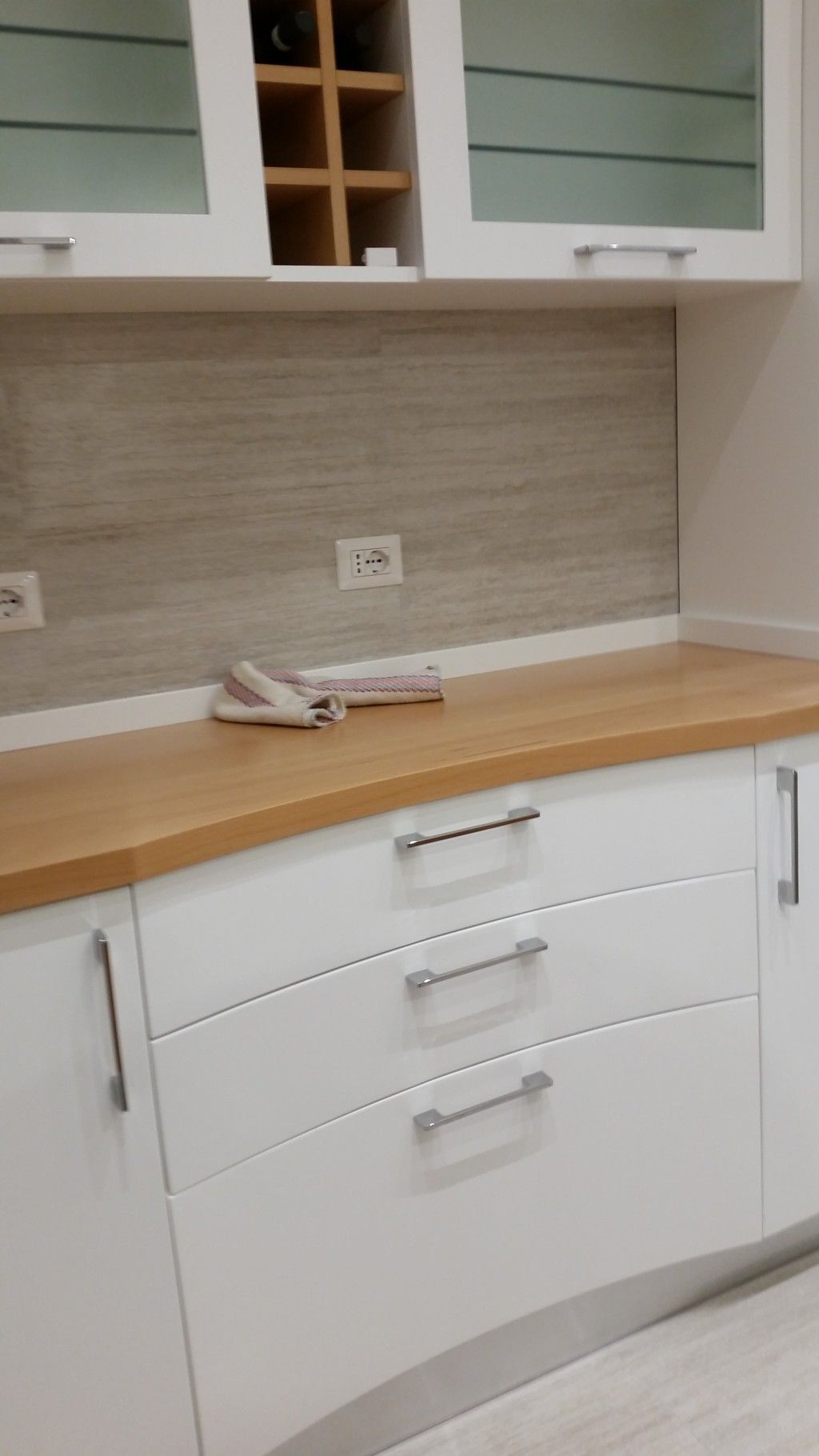 Bancone da cucina moderno con mobili bianchi, piano di lavoro in legno e paraschizzi in piastrelle grigie.
