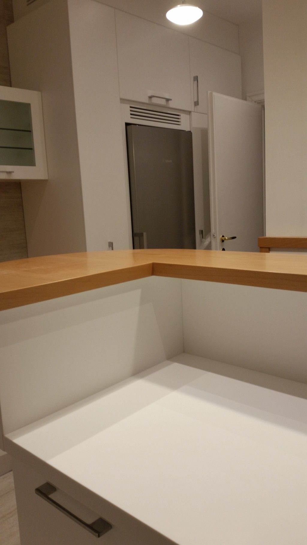 Bancone da cucina bianco con finiture in legno e porta aperta che conduce a un corridoio sullo sfondo.
