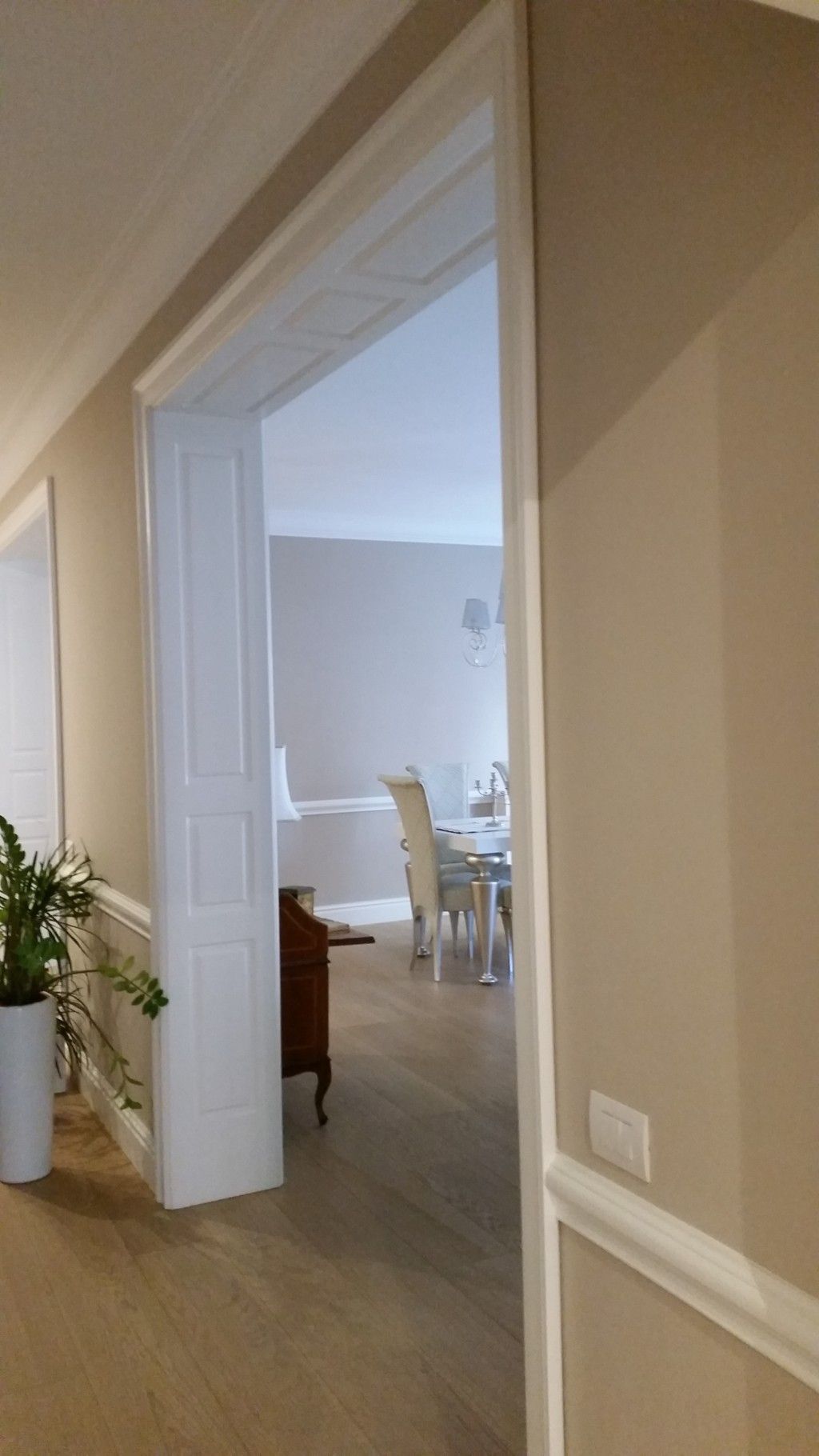 Si apre una porta su una luminosa sala da pranzo con sedie bianche e pavimento in legno.