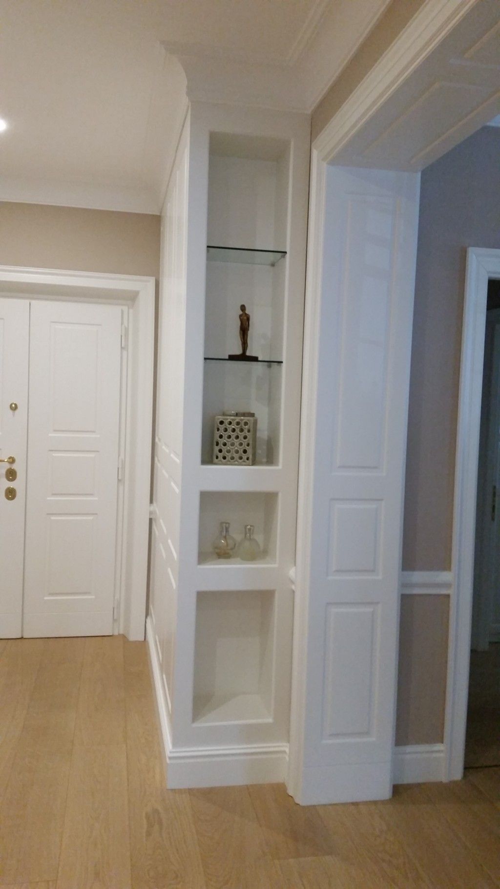 Corridoio con mensole a muro bianche che espongono piccoli oggetti decorativi accanto a una porta.