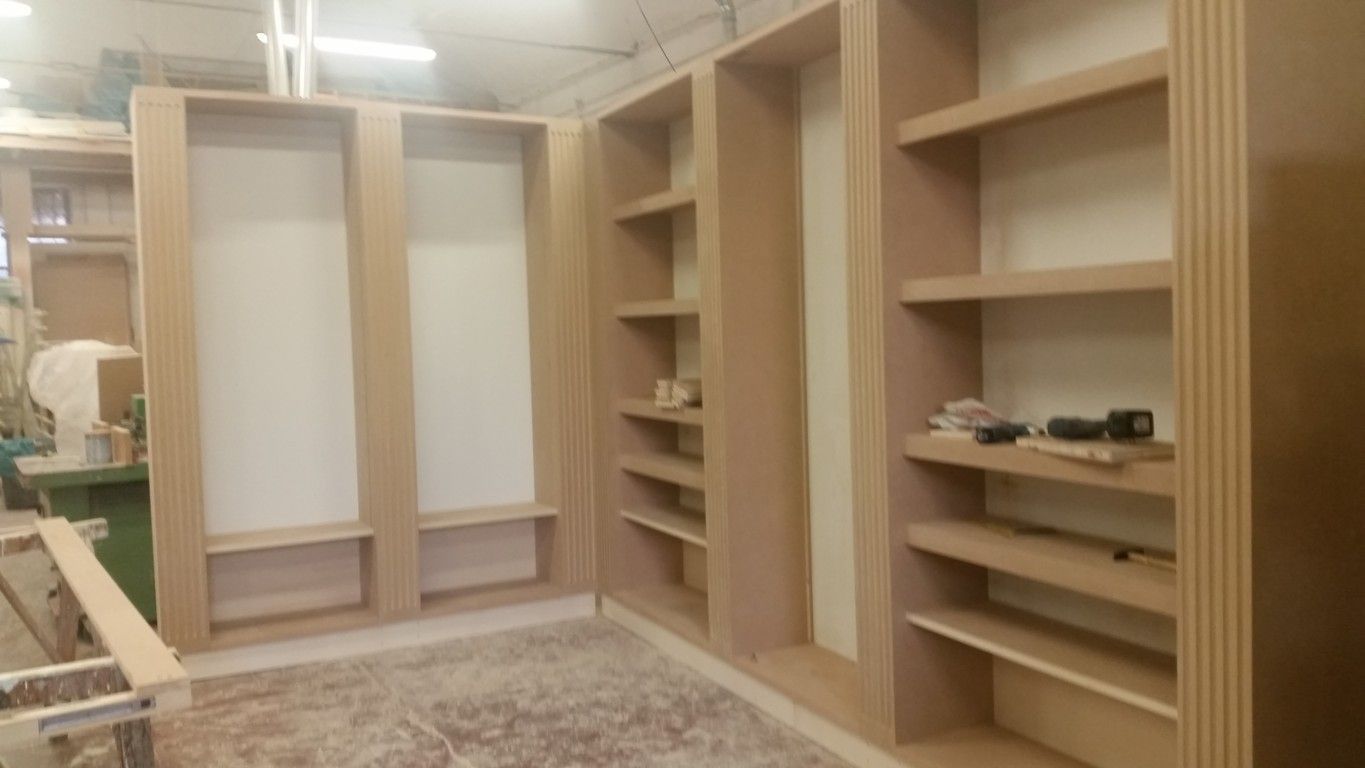 Armadio a muro con scaffalature in legno, scomparti a giorno e aste appendiabiti, in una stanza con moquette.