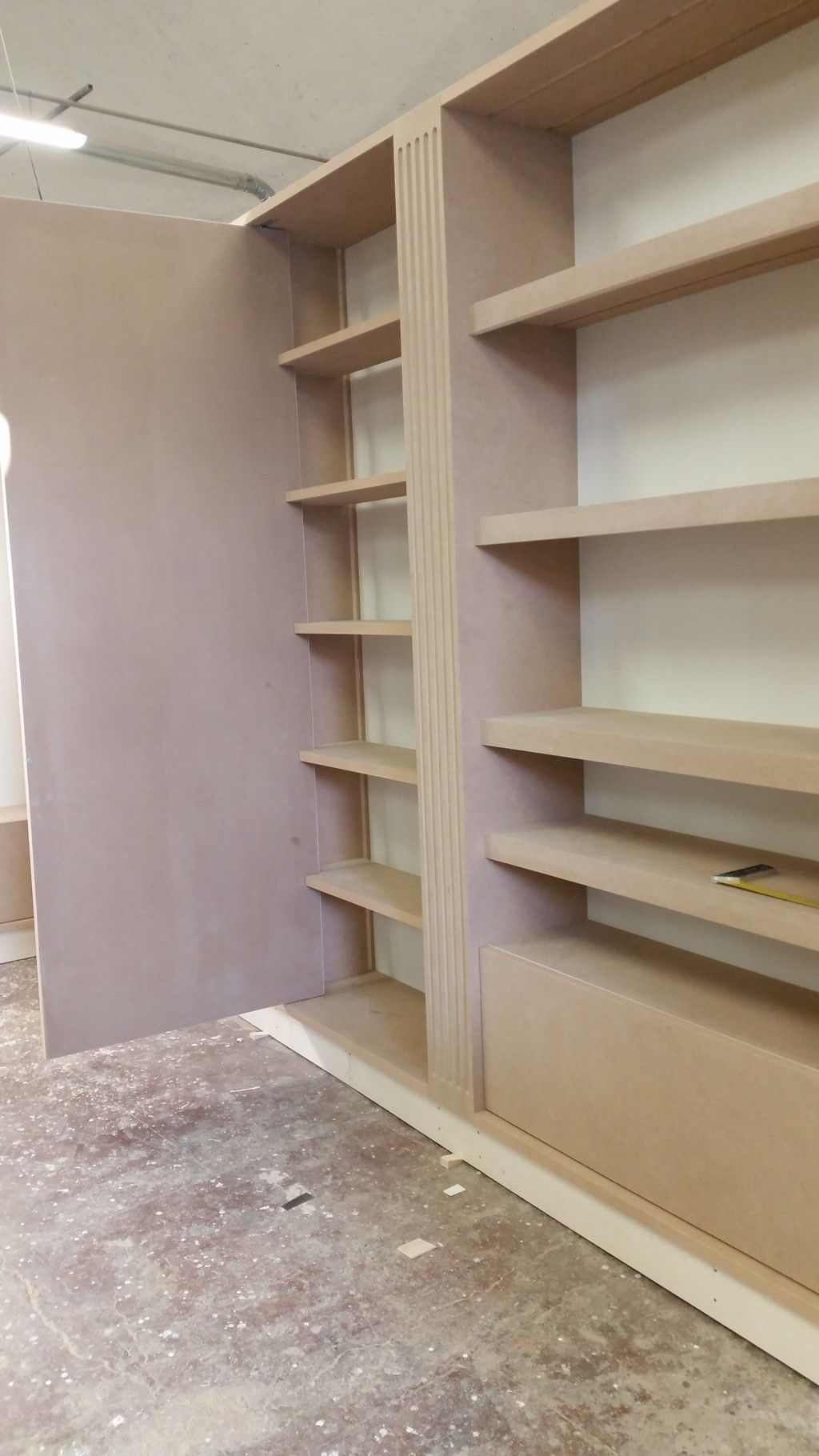 Scaffalatura a muro in legno beige in una stanza non rifinita con pavimento polveroso.
