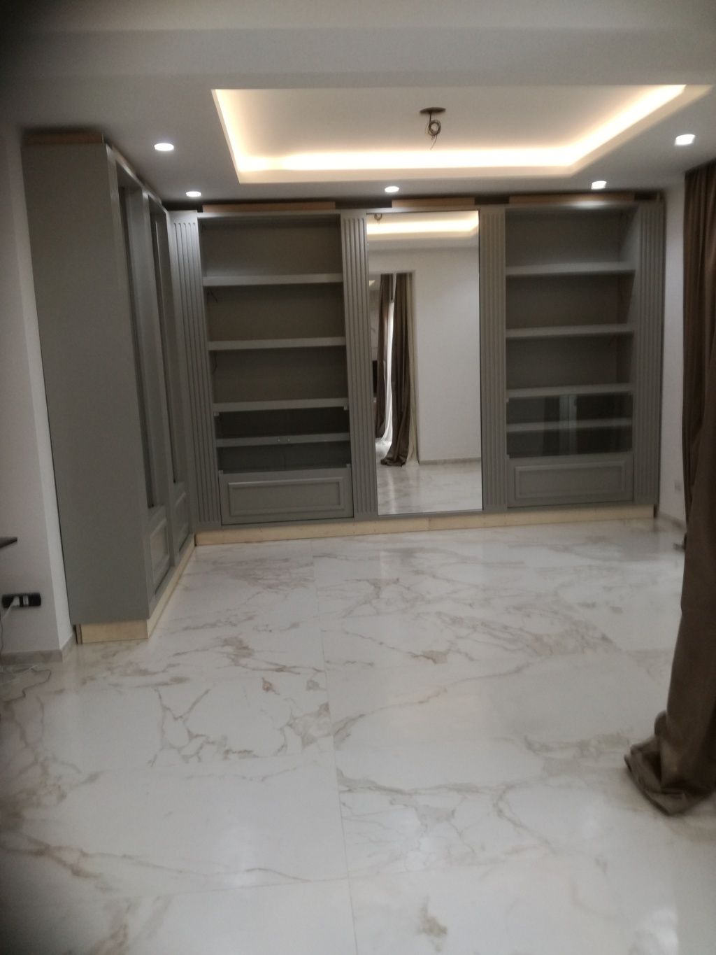 Cabina armadio moderna e vuota con scaffali a muro, pavimento in marmo bianco e faretti a incasso a soffitto.