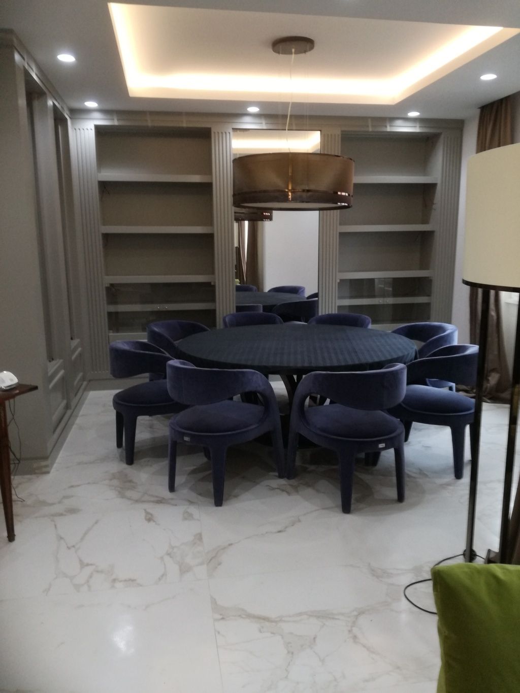 Sala da pranzo moderna con tavolo rotondo, sedie blu, scaffali a muro e pavimento in marmo.