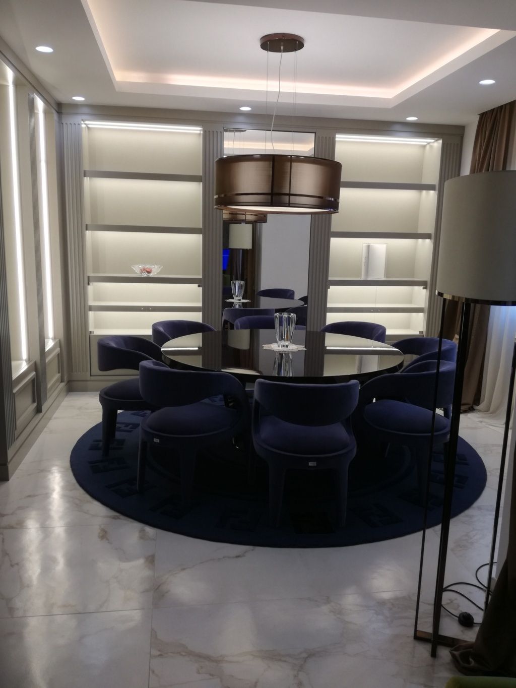 Sala da pranzo moderna con tavolo rotondo, sedie scure e una grande lampada a sospensione, in tonalità neutre.