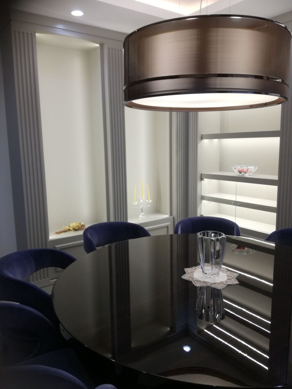 Elegante sala da pranzo con tavolo rotondo nero, sedie blu e una grande lampada a sospensione in bronzo.