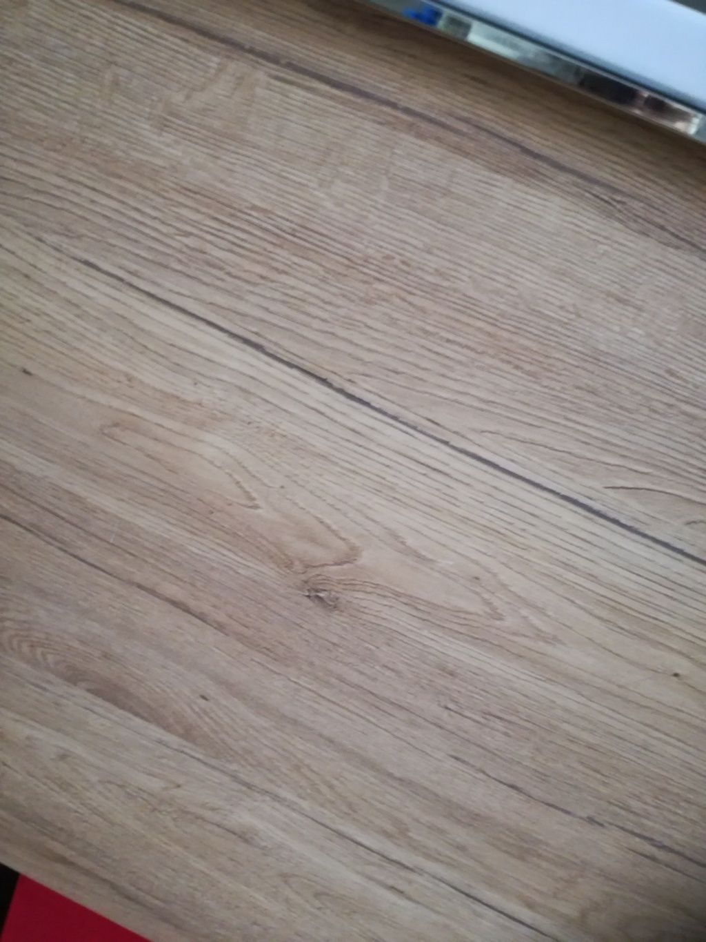 Primo piano di un pavimento in legno chiaro con venature diagonali e bordo argentato nella parte superiore.