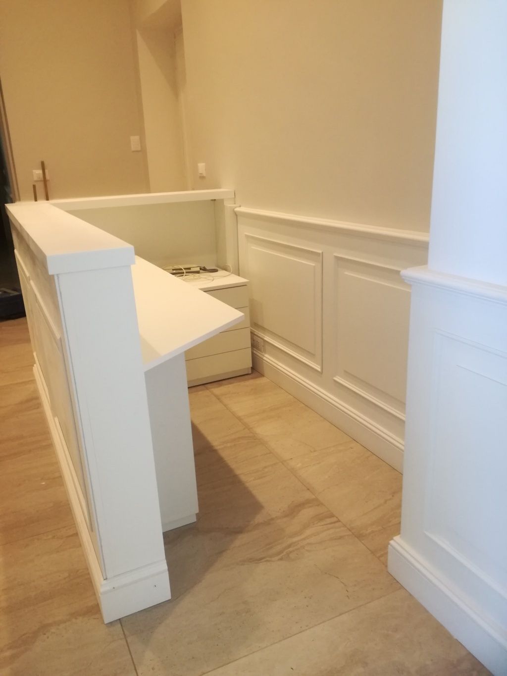 Corridoio vuoto con pareti beige, finiture bianche e una piccola scrivania o mensola bianca vicino al pianerottolo delle scale.