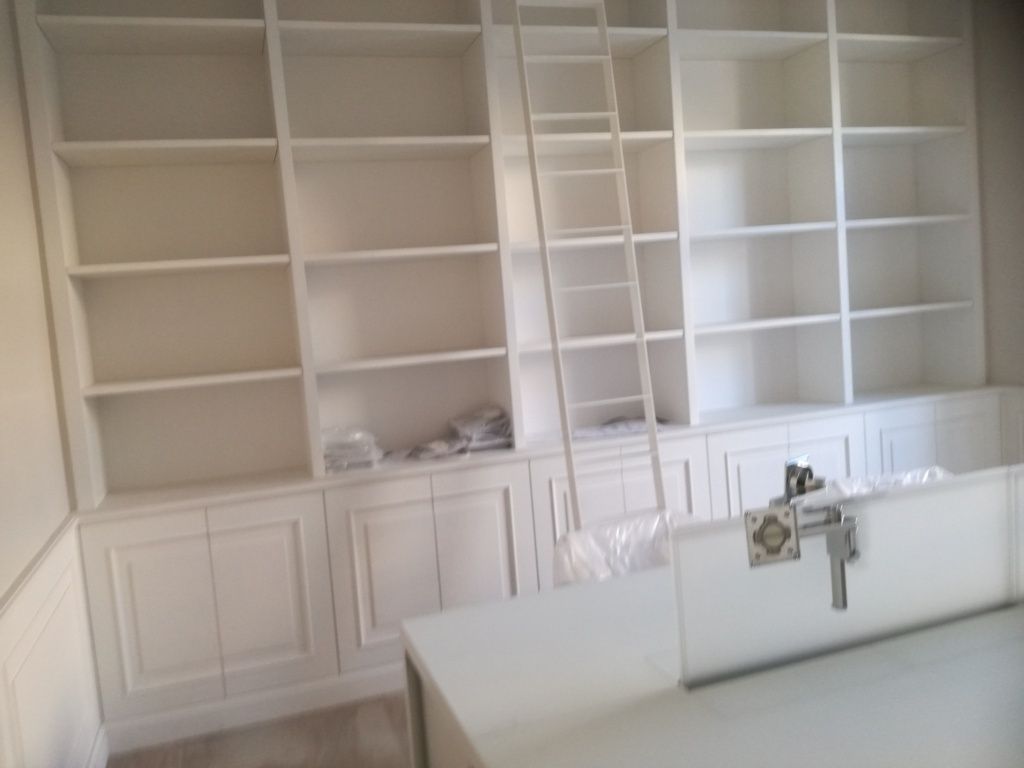 Armadi a muro bianchi e mensole a vista in una stanza luminosa, con un lavabo in primo piano.
