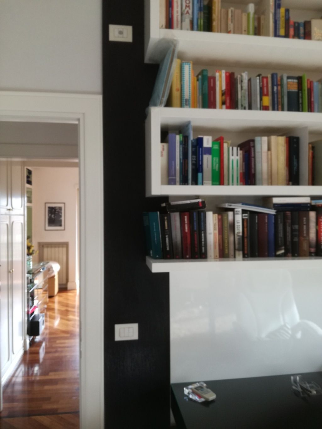 Soggiorno moderno con scaffali bianchi per libri, una parete d'accento nera e un corridoio con pavimento in legno.
