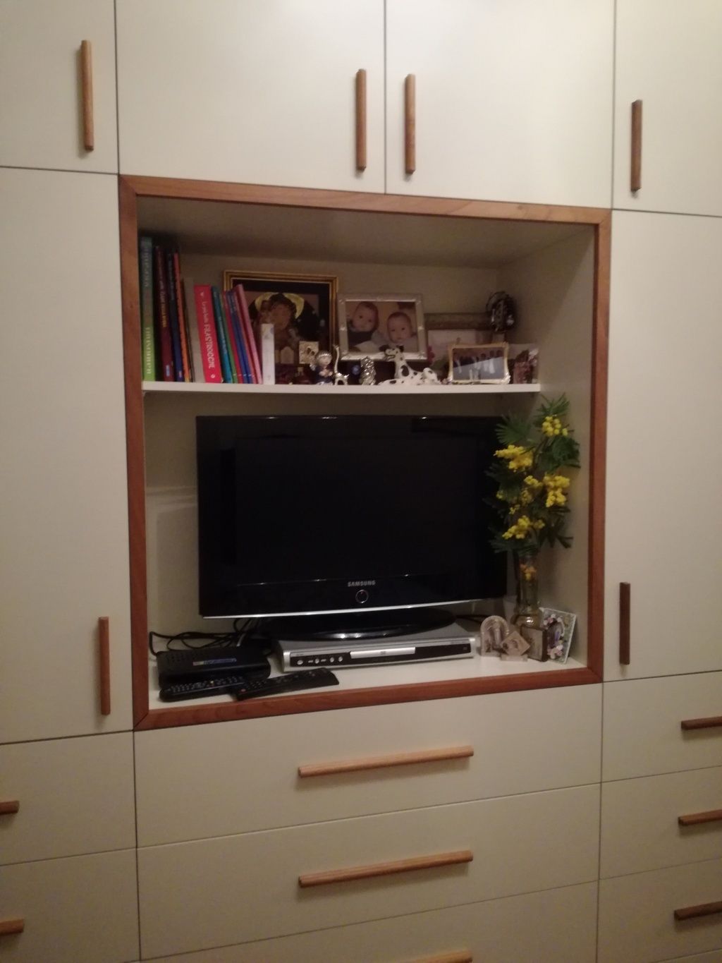 Mobile per l'intrattenimento in soggiorno con TV, foto incorniciate, libri e composizione floreale.