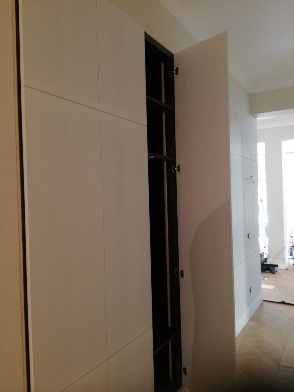 La porta di un armadio aperta in un corridoio bianco rivela un interno buio.