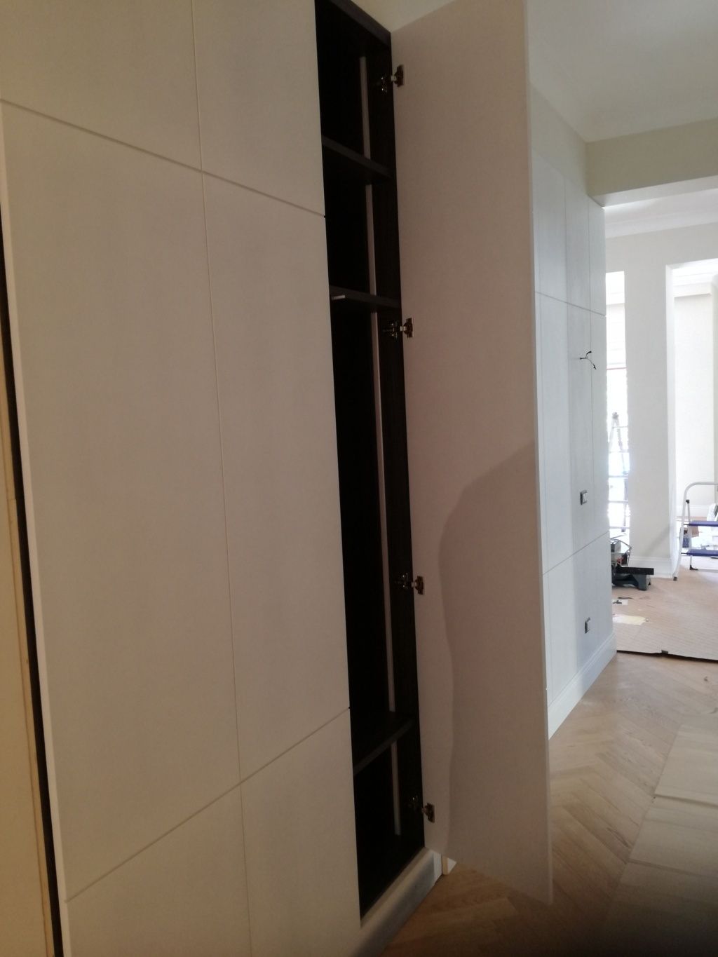 Nicchia stretta a muro in un corridoio bianco, con alte mensole scure e uno spazio aperto visibile oltre.
