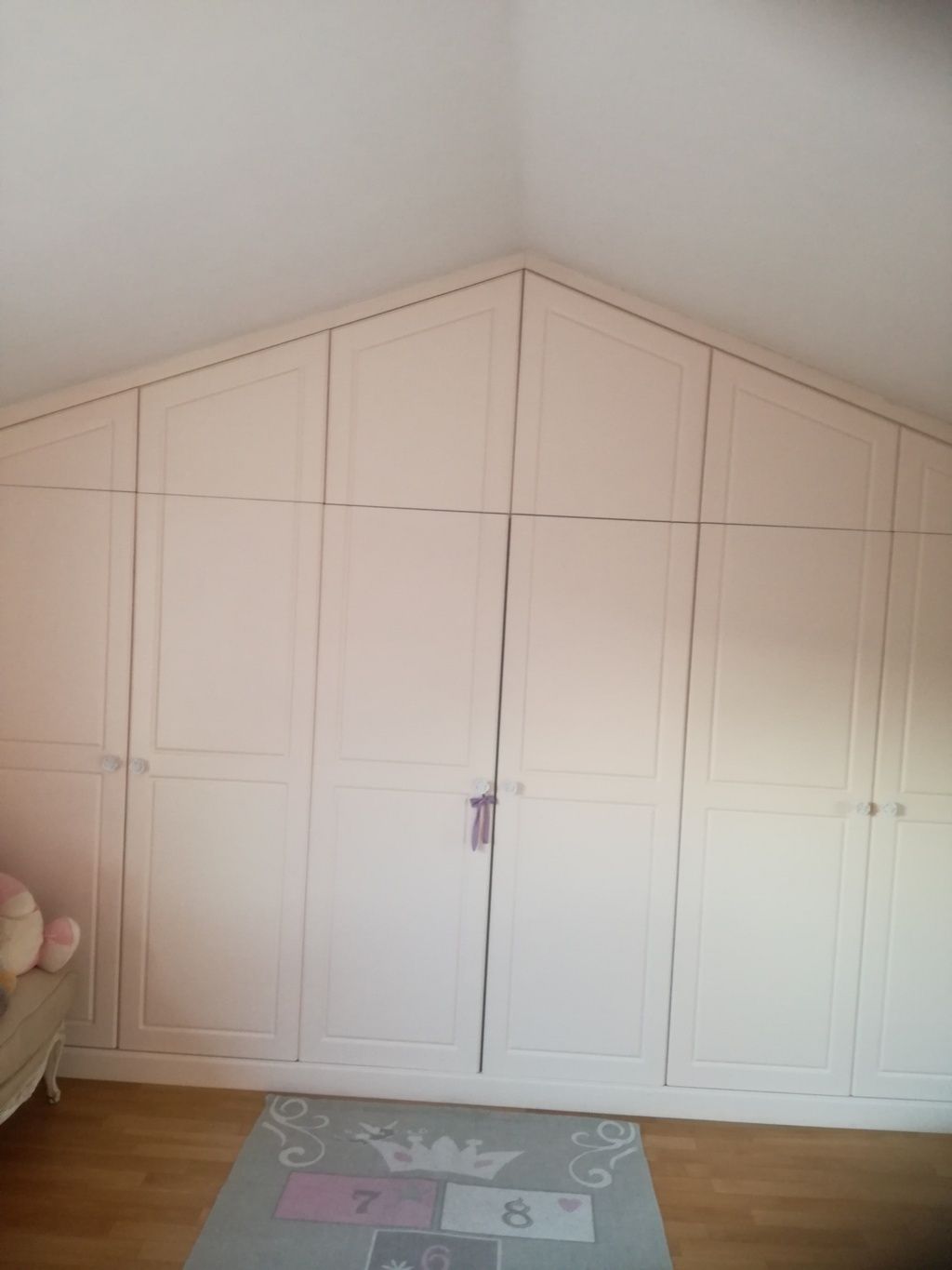 Armadio a muro rosa integrato nella parete con soffitto inclinato in una piccola camera da letto.