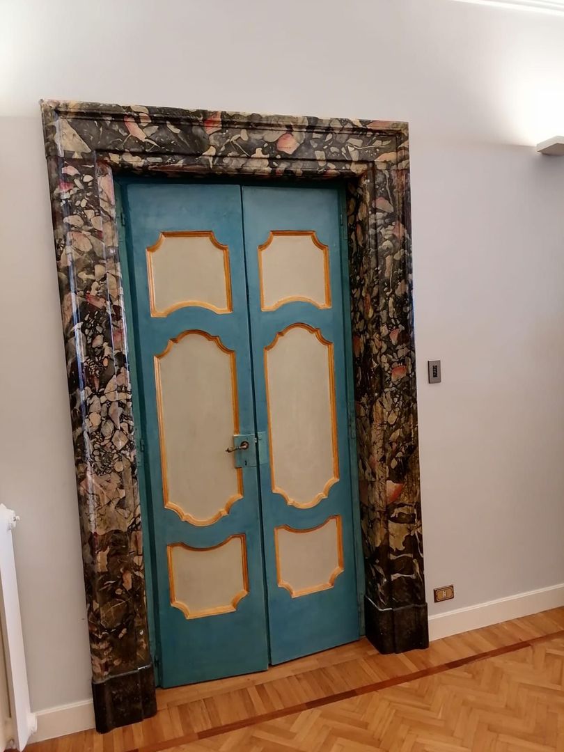 In una stanza dalle pareti bianche, doppie porte blu incorniciate da una cornice di marmo scuro riccamente decorata.