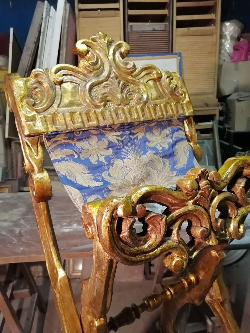 Sedia decorata con vernice dorata e rivestimento in tessuto blu a motivi geometrici, in un'area di stoccaggio di un'officina della famiglia dei