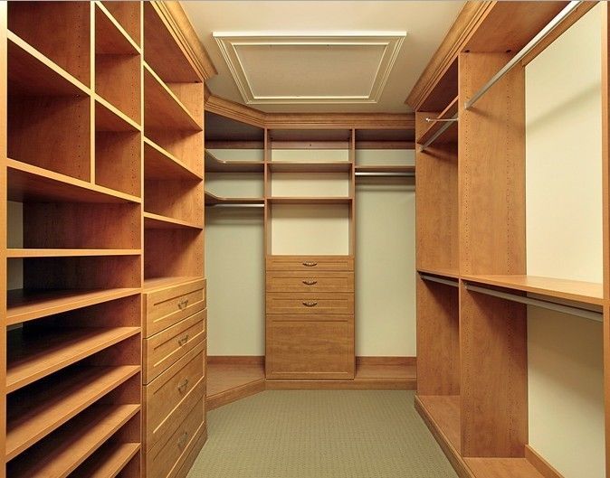Cabina armadio con ripiani, cassetti e appendiabiti in legno in una stanza beige.