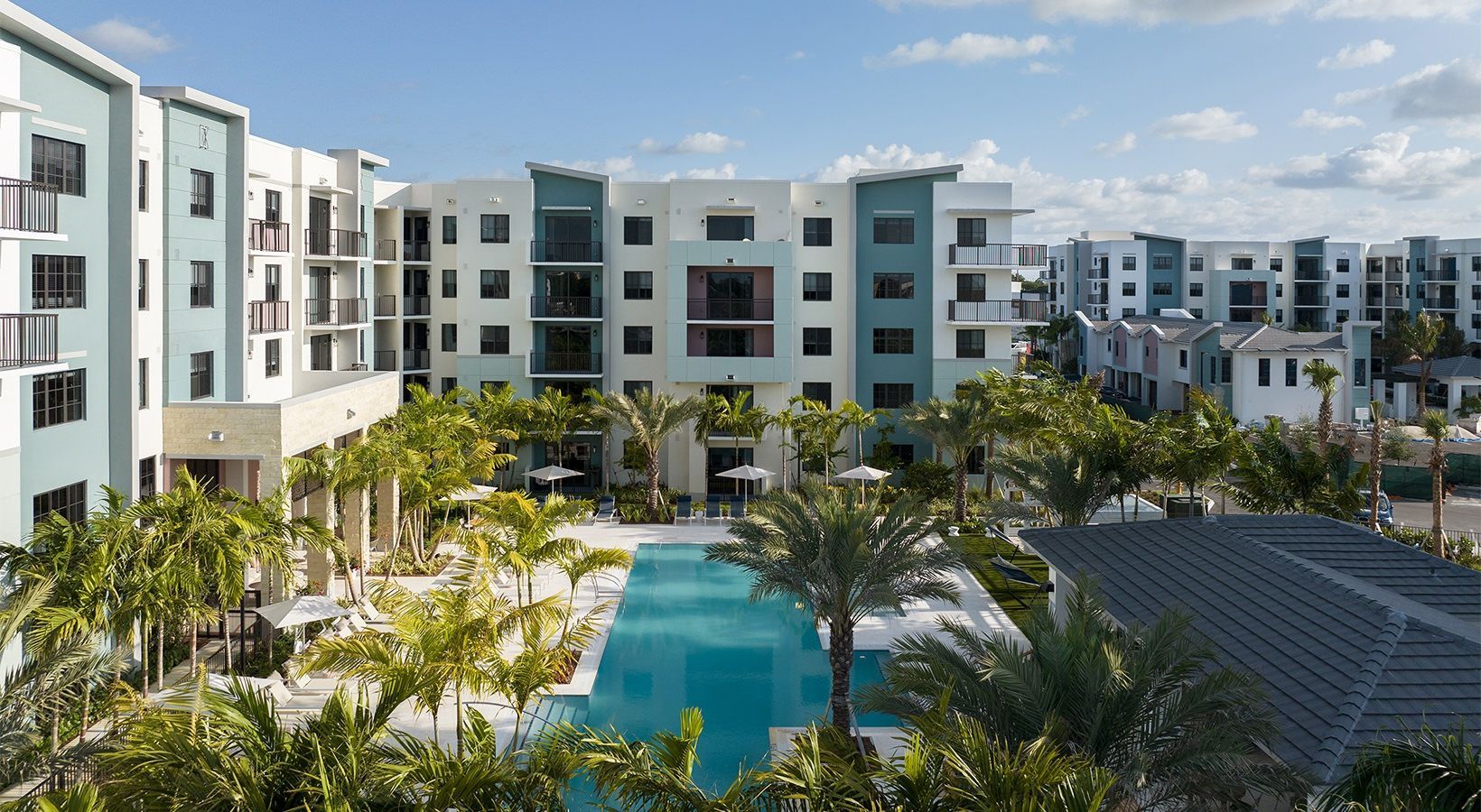 Modern apartment complex with a central swimming pool and palm trees under a clear blue sky