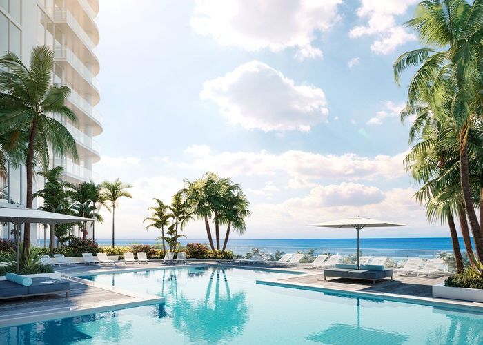Luxury resort pool overlooking a sunny ocean with palm trees and lounge chairs