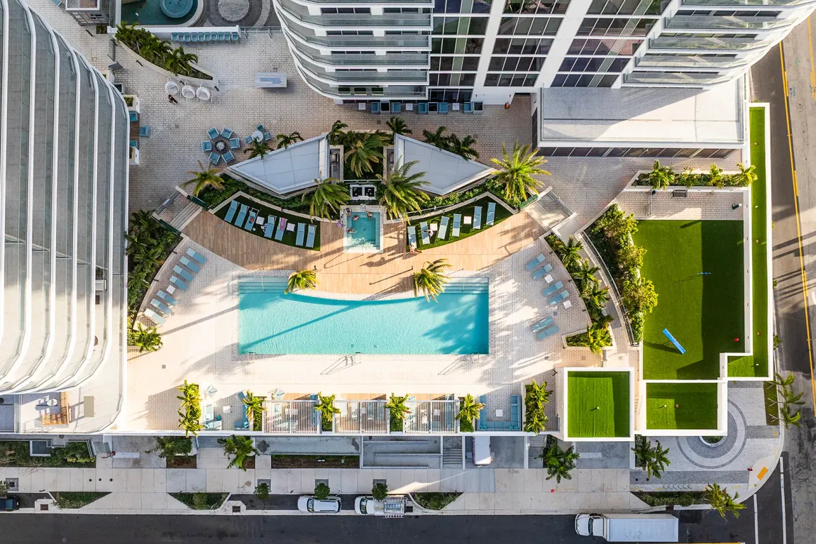 Aerial view of a modern apartment courtyard with a swimming pool, lawns, and rooftop terraces.