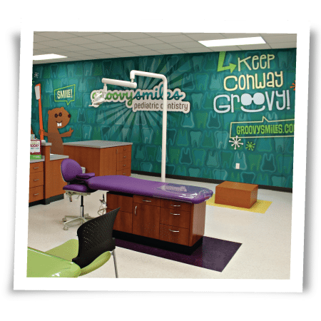 Pediatric dentist office with a purple chair, cartoon wall art, and the words 