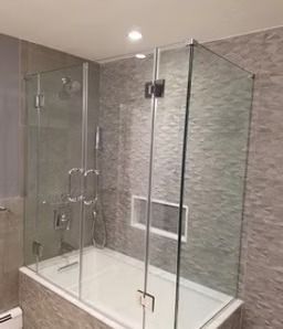 Modern glass shower enclosure with hinged door, chrome handles, and gray tile bathroom walls